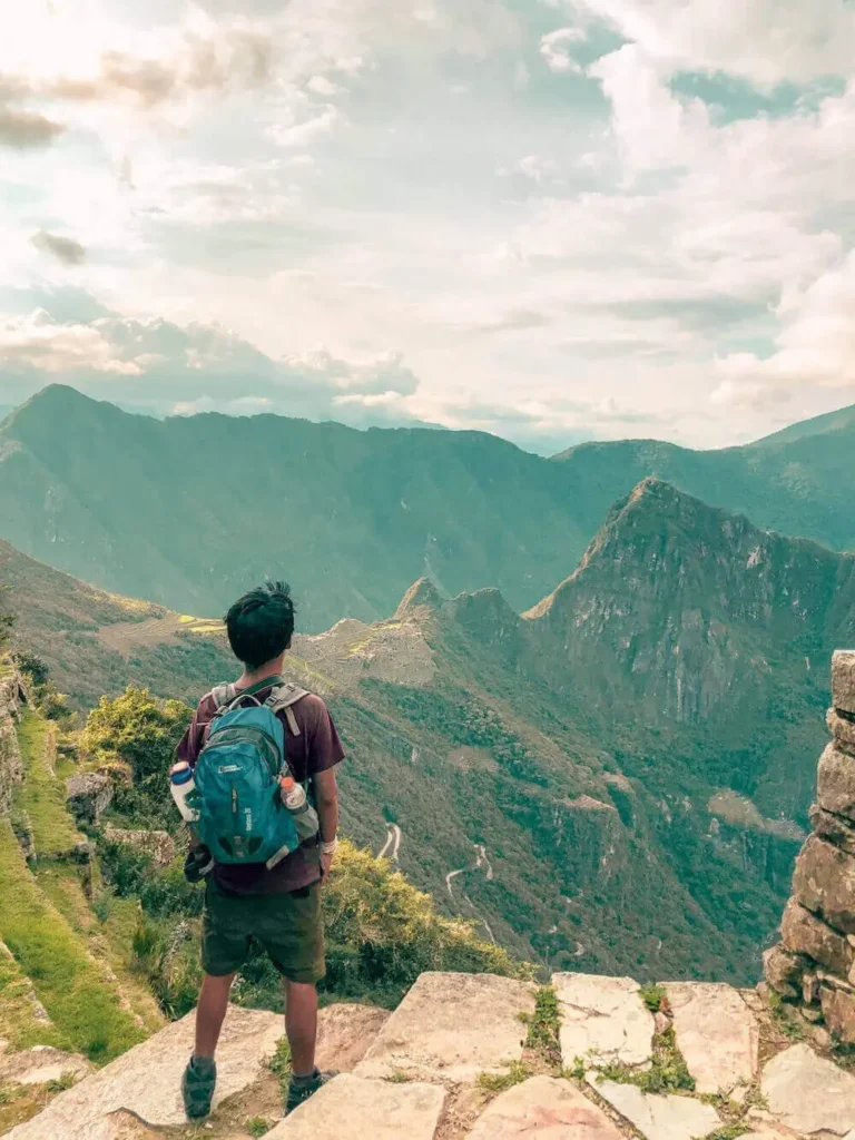 Trekker standing at a mountain viewpoint looking down at ancient ruins at dawn
