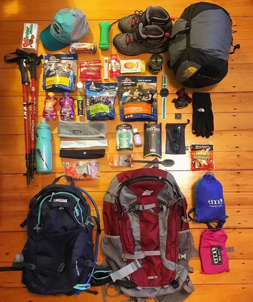 Hiking gear laid out including boots trekking poles thermal layers and daypack for mountain trek