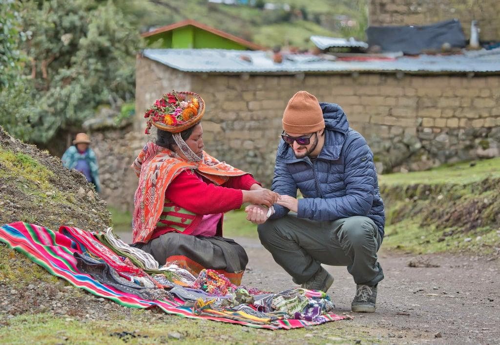 Trekker purchasing handwoven textile directly from Quechua artisan woman in mountain village