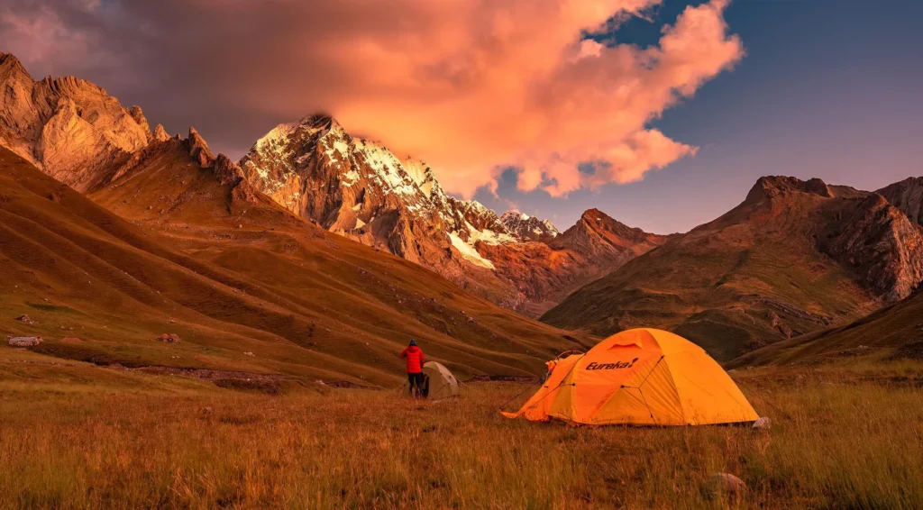 Campsite at high altitude with mountain tents and snow-capped peaks visible at sunset